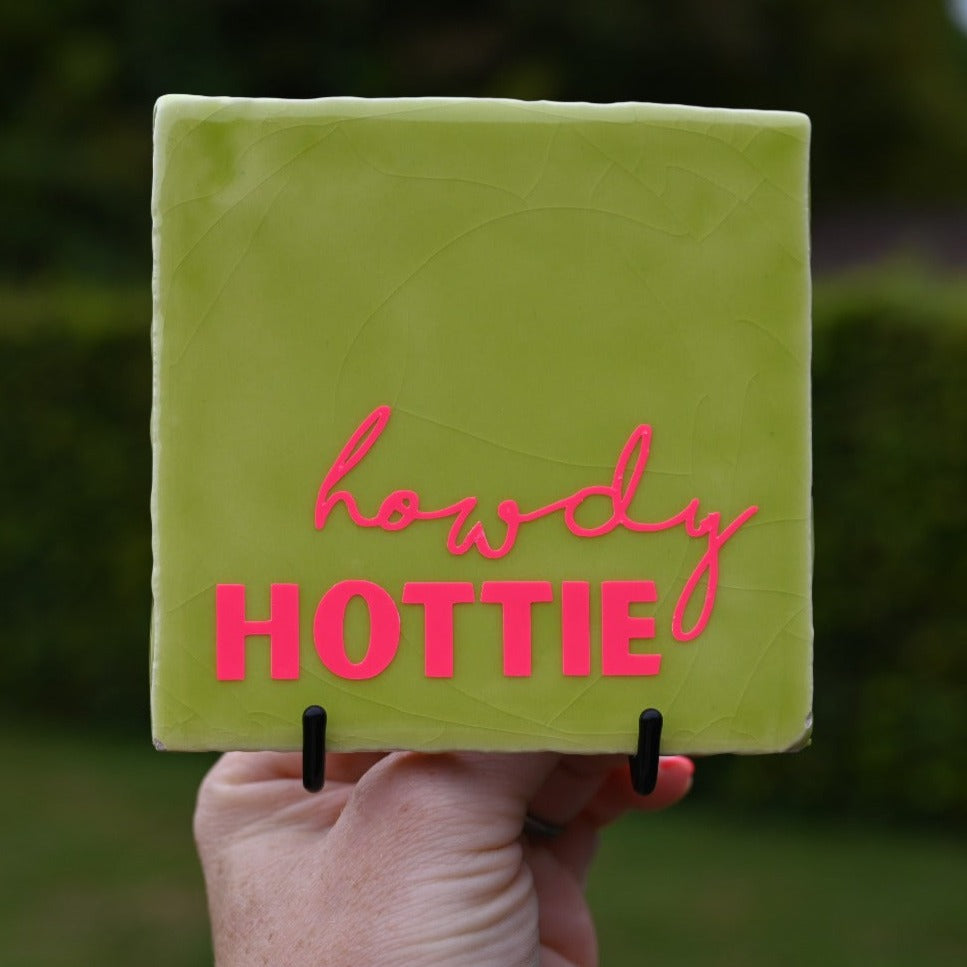 Voorbeeld van zwarte tegelhouder met lime gekleurde quote tegel met de roze tekst "Howdy hottie" in de hand. 