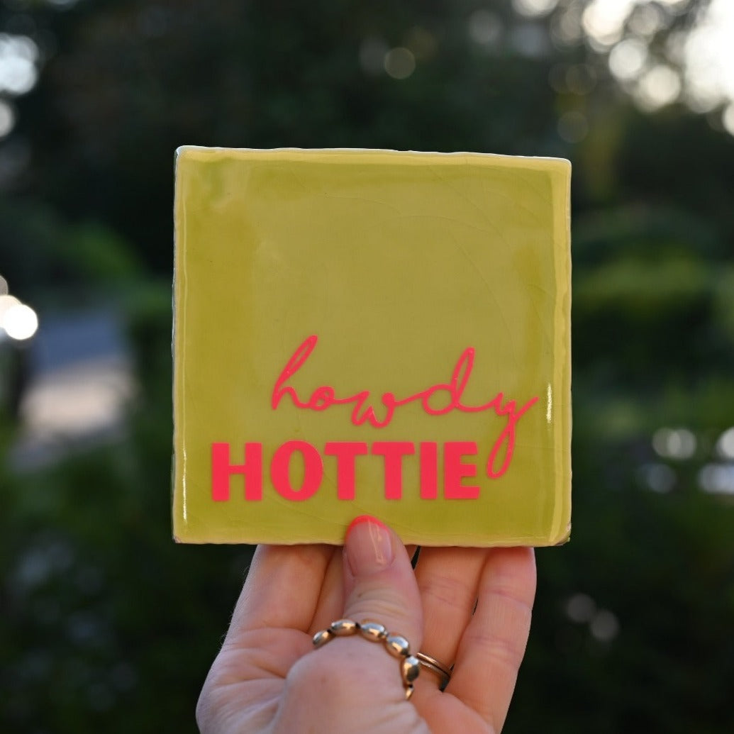 Mooie standaard quote tegel met tekst "Howdy hottie" in de hand.  Tegelkleur lime met roze tekst opdruk. Schitterend in het licht. Geheel zelf te kiezen in allerlei kleurencombinaties.