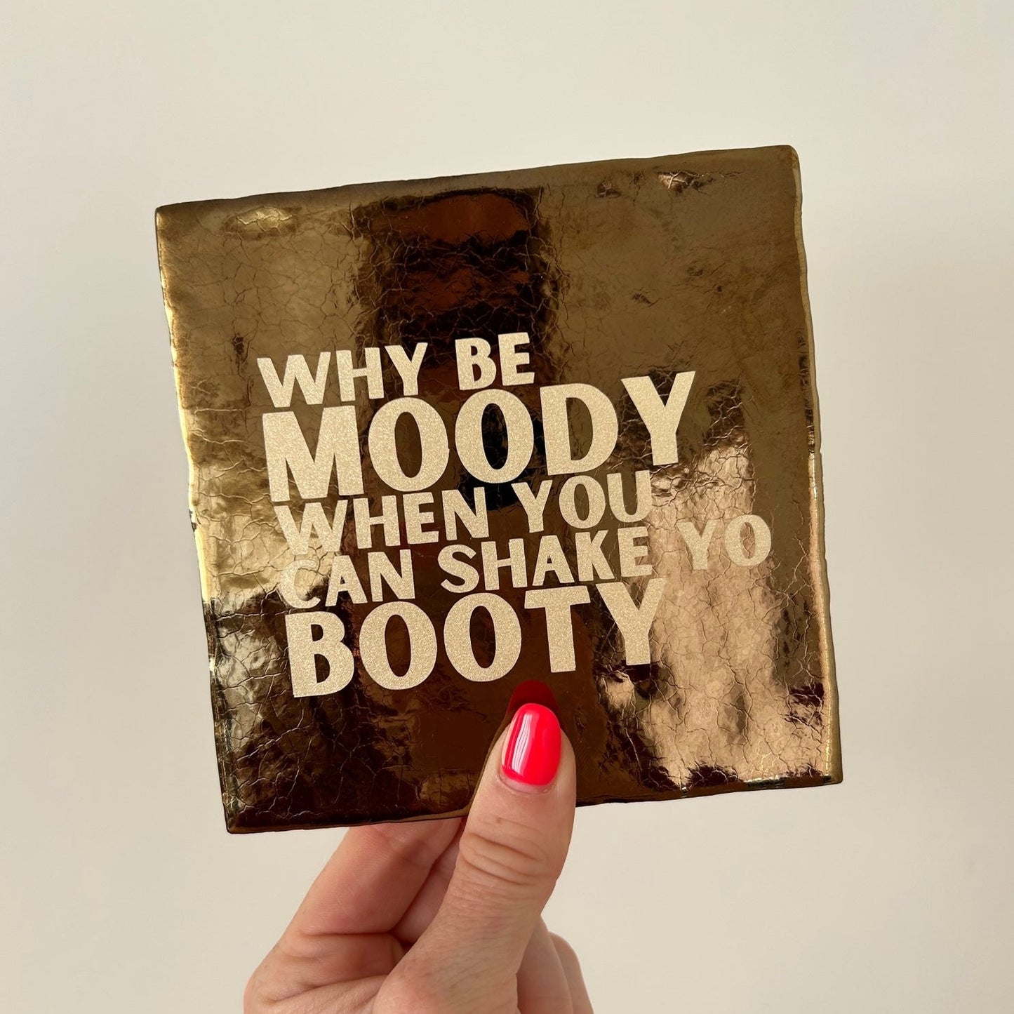 Mooie standaard quote tegel met tekst "Why be moody when you can shake yo booty" in de hand.  Tegelkleur goud met gouden tekst opdruk. Schitterend in het licht. Geheel zelf te kiezen in allerlei kleurencombinaties.