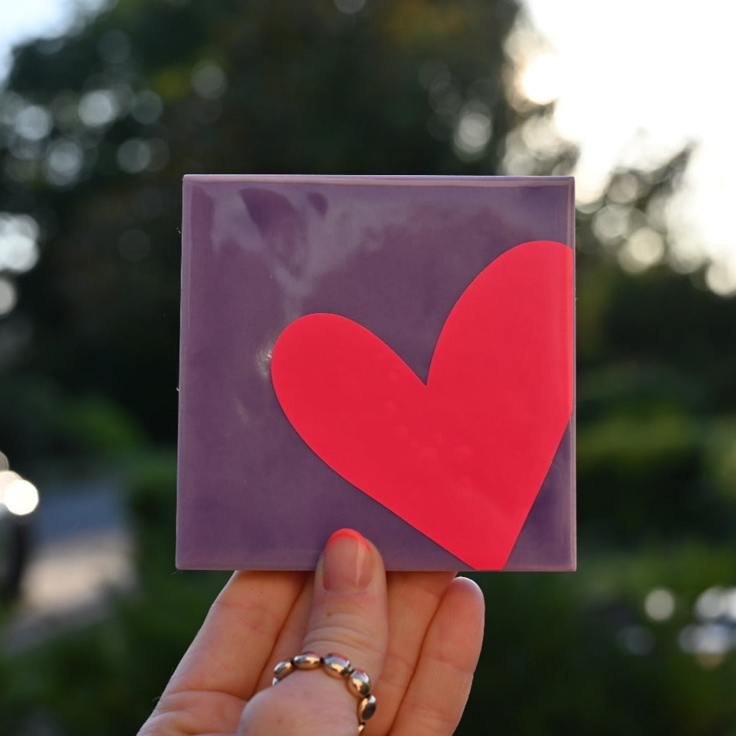 Mooie standaard tegel met hart in de hand. Tegelkleur paars met roze opdruk. Schitterend in het licht. Geheel zelf te kiezen in allerlei kleurencombinaties.