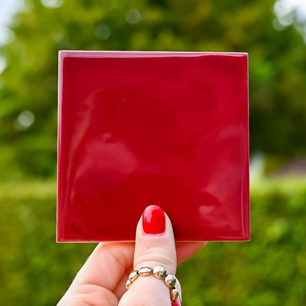 Mooie burgundy gekleurde tegel in de hand in de lucht. Voor jou personaliseren wij deze met liefde