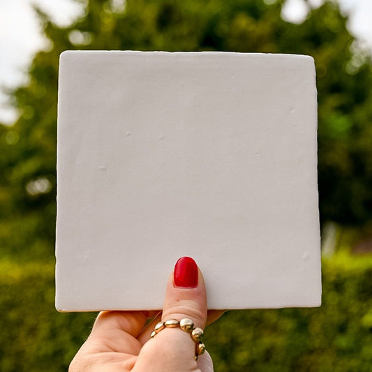 Mooie mat witte tegel in de hand in de lucht. Voor jou personaliseren wij deze met liefde. 