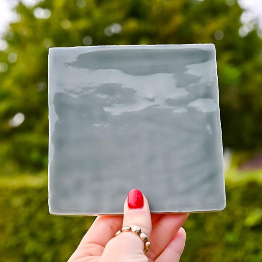 Mooie grijsgroen gekleurde tegel in de hand in de lucht. Voor jou personaliseren wij deze met liefde