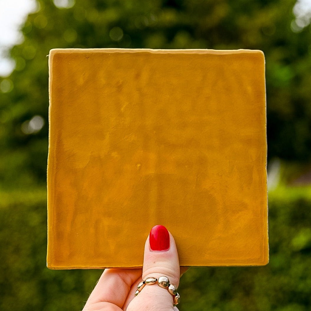 Mooie oker gekleurde tegel in de hand in de lucht. Voor jou personaliseren wij deze met liefde