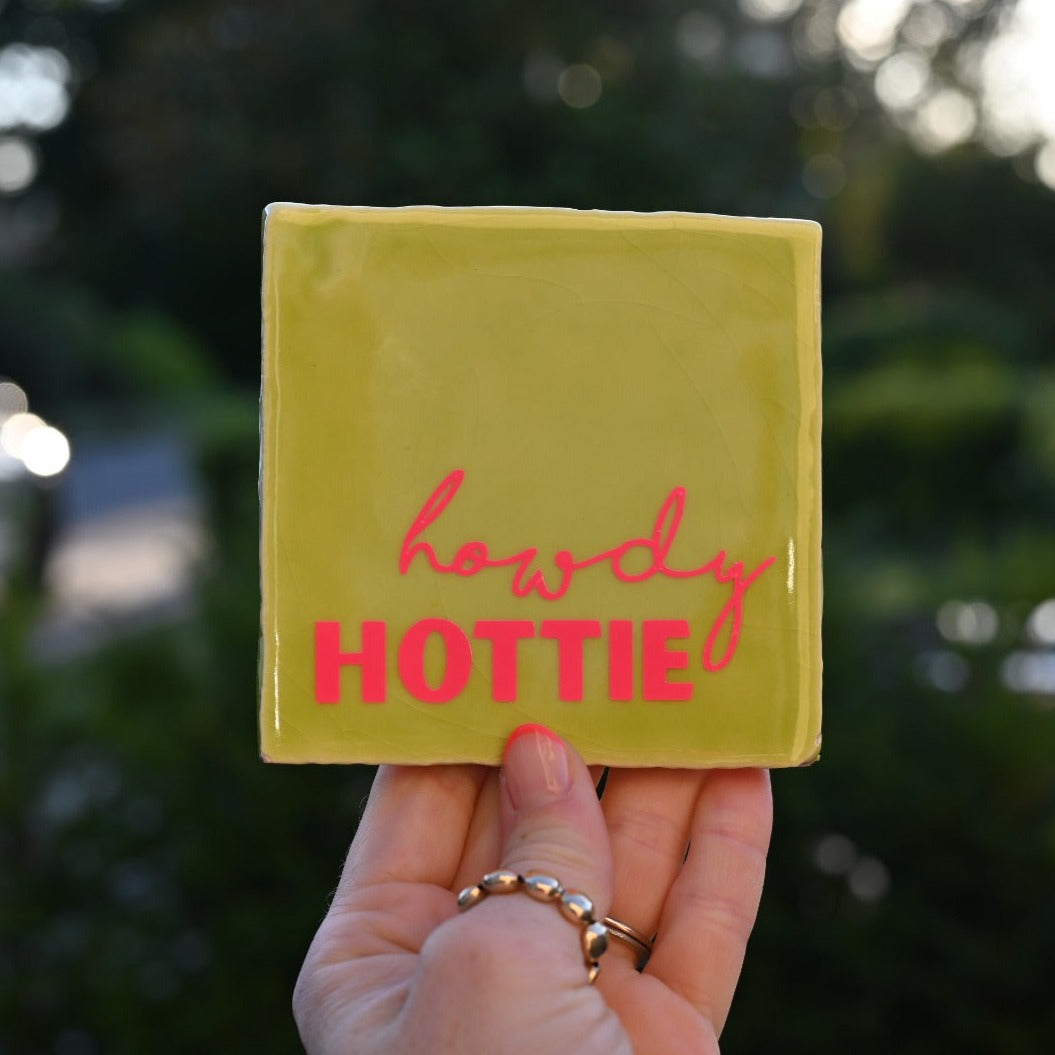 Mooie standaard quote tegel met tekst "Howdy hottie" in de hand.  Tegelkleur lime met roze tekst opdruk. Schitterend in het licht. Geheel zelf te kiezen in allerlei kleurencombinaties.